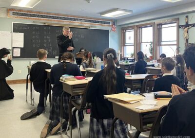 5th graders kneel by their desks to receive the blessing of the bishop.